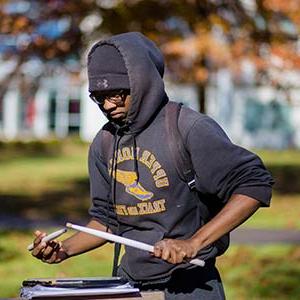 Student drumming on a notebook outside in the fall